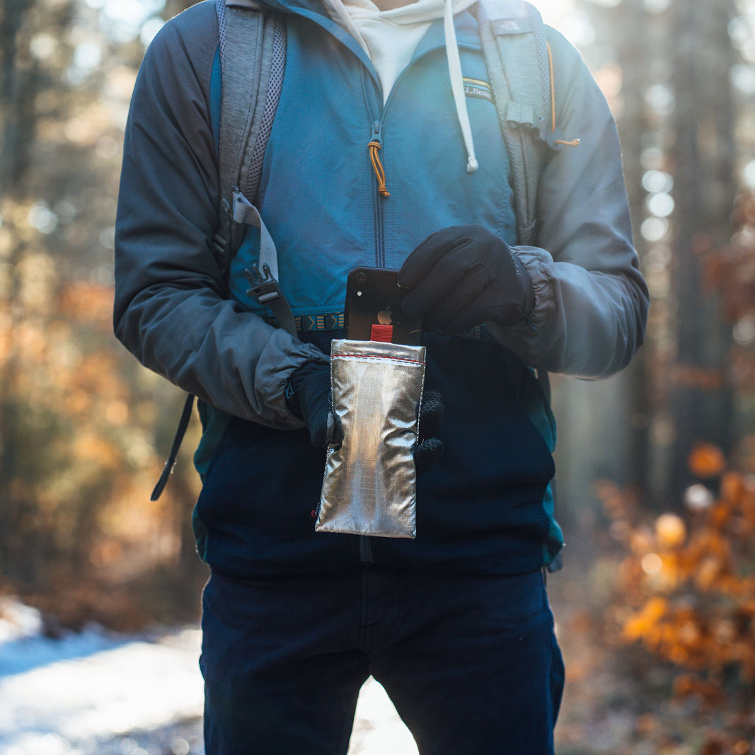 Man removing his phone from an Apollo PHOOZY Thermal Capsule on a snowy winter trail, protecting it from cold weather